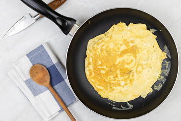 Flatlay above fried omelet in the frying pan with dishcloth on the table