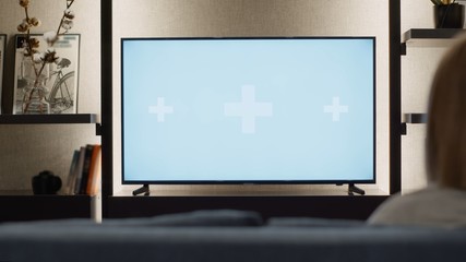 Over shoulder view of young woman relaxed at home watching television TV green white screen mock-up...