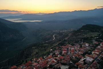 Aerial view of Delphi, Greece, the Gulf of Corinth, orange color of clouds, mountainside with layered hills beyond with rooftops in foreground