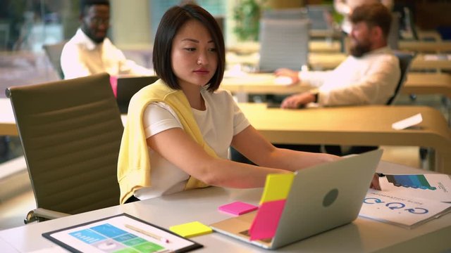 Asian female employee in smart casual clothing working with paper documents and laptop information, Chinese woman professionale planning productive organisation while analyzing startup project