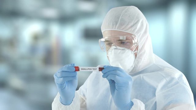 A laboratory assistant wearing protection gear examines vial with smallpox blood test