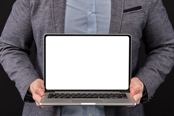 A man in a jacket holding a laptop with copy space on a black background.