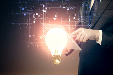 Double exposure of man's hands holding and using a digital device and bulb hologram drawing. Idea concept.