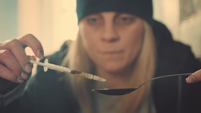 Addict woman with syringe and spoon preparing dose of narcotics in an abandoned house. Social degradation