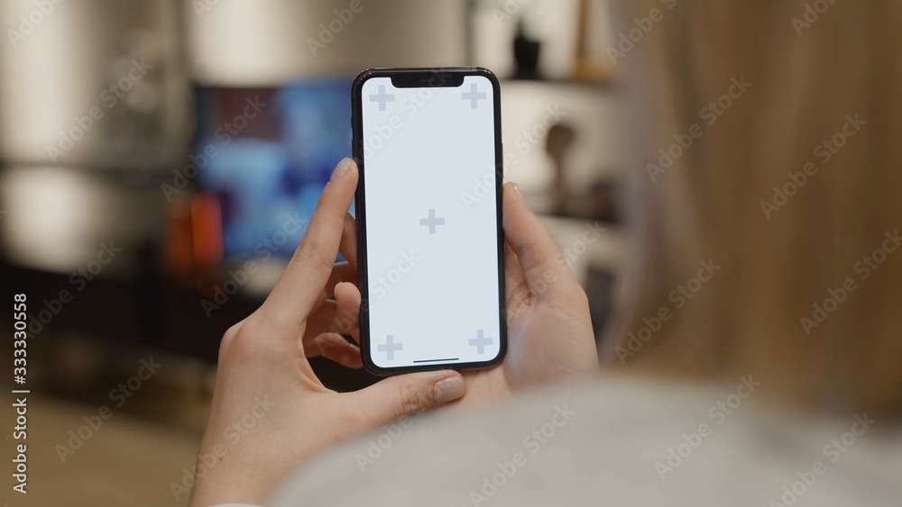 Wall mural over shoulder view of woman at modern room uses smartphone hold in both hands with green white scree