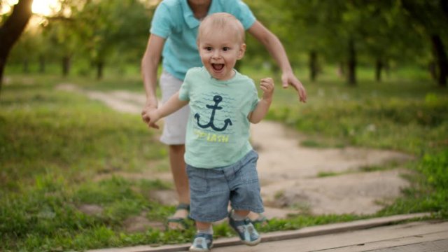 Cute brothers walking in park. Elder brother hel junior to make steps outdoors