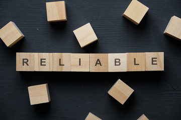 Modern business buzzword - reliable. Top view on wooden table with blocks. Top view.