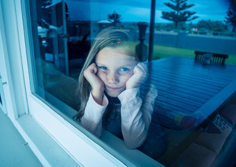 COVID-19 Quarantine. Sad little girl looking through the window feeling lonely during lockdown