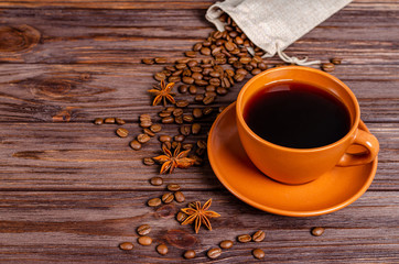 Cup of black aromatic coffee in a clay cup with anise stars and cinnamon sticks on a wooden background