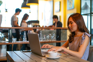 Asian woman using laptop computer online learning and working from coffee shop. work from home, online learning, self studying, digital technology, digital studying or online marketing concept