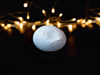 a broken white egg on a black festive background with a bokeh of their garlands