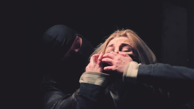 A masked man closes his mouth to a woman. Fear of woman victim of domestic violence and abuse. Violence, crime and kidnapping concept