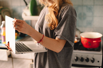 Woman using laptop computer while cooking food on kitchen