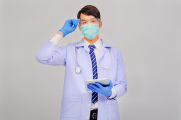 Medical doctor in white uniform doctor wears medical gloves, medical masks and and wearing protective glasses holding tablet on gray background, corona virus concept, covid19 concept, medical concept