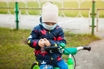child on a walk in a city park in a medical mask on a bicycle. Hand treatment with antiseptic. Walking on the street during the quarantine period of the coronavirus pandemic in the world