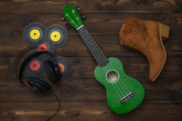 Naklejka premium Green ukulele, headphones, suede boot and vinyl discs on a wooden background.