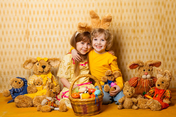brother and sister with hare ears and toys hares are sitting with a basket full of Easter eggs. family holiday at home.