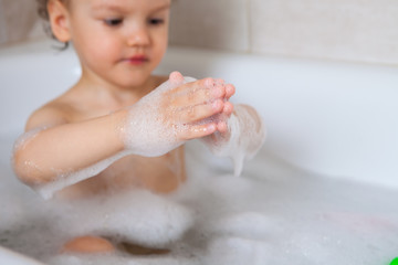 Fototapeta premium hygiene. the child bathes in a bath with foam. Washing a child after a walk on the street. Hands in foam close up.