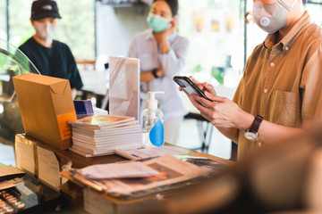 Women in protective face mask placing an order with cell phone at cafe counter.