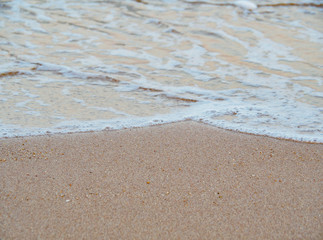 Golden sand on tropical beach near sea. Sea surf close up with soft waves on sunset. Sandy beach, background for travel and holiday.