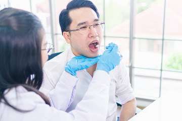 Fototapeta premium Attractive female doctor taking a saliva sample from asia man mouth with a cotton swab.man chech body during the virus eqidemic
