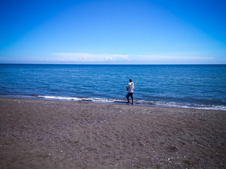 Peaceful Beach Scenery With A Man Standing Fishing At The Seaside On A Sunny Clear Blue Sky At The Village, Umeanyar, North Bali, Indonesia