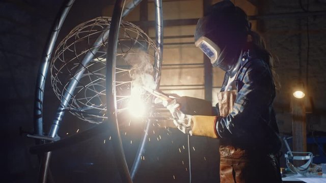 Talented Emerging Female Artist is Welding an Abstract, Brutal Metal Sculpture that Reflects the Present Moment. Beautiful Tomboy Fabricator in Checkered Shirt Creating Modern Steel Art.