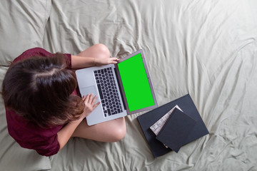 Young woman drinking coffee in her bed and checking her laptop, top view