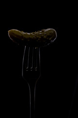 The whole canned cucumber, planted on a fork, located vertically on a black background, stroke with outline light