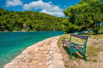 A rustic wooden and wrought iron bench sits empty beside a stone walking path on St. Mary's Island...