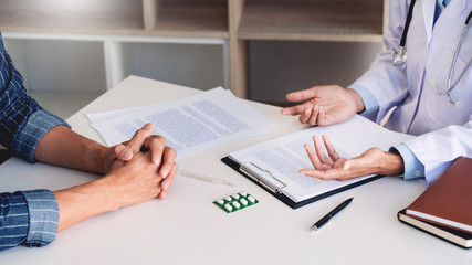 patient listening intently to a male doctor explaining patient symptoms or asking a question as they discuss paperwork together in a consultation
