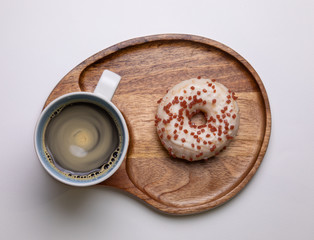 Donuts topped with icing sugar and sprinkled with sugar, pink flakes placed on a wooden plate looks delicious with one cup of hot black coffee for the breakfast which gives the energy and freshmen