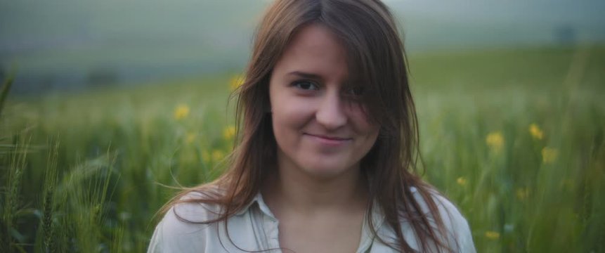 A young woman with long brown hair in a middle of a green wheat field, smiling, feeling happy. CLOSE UP, SLOW MOTION, SHALLOW DOF. Freedom, lifestyle concept. BMPCC 4K 
