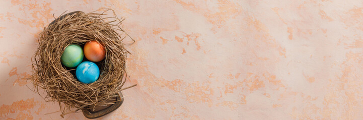 Easter eggs in a bird's nest on a textural background. Easter celebration concept. Copy space. Flat lay. Banner.