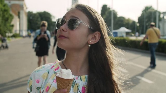 Relaxed girl walking in amusement park. Teen girl eating ice cream cone