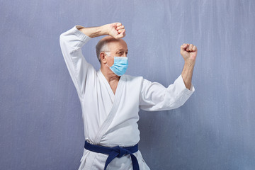 In a medical mask and karategi, an old man trains a punch