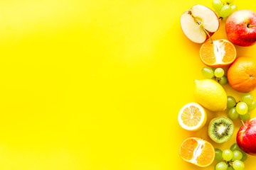 Fresh fruits background with citruses, apple, kiwi and grape on yellow table top-down frame copy space