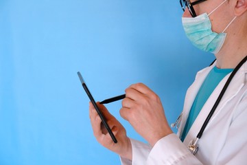Medicine concept.Medical technology.Doctor  in a mask and in a white coat with a tablet in hands close-up on a blue background. The fight against viruses.Caronavirus epidemic statistics