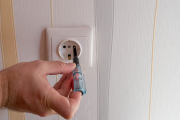 Man's hand holds handle of indicator screwdriver, that is inserted into electrical outlet,...