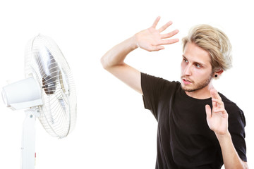 Young man fighting with wind from cooling fan