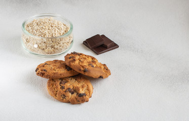 Gluten free homemade oatcookies,oat flakes in a jar and pieces of dark chocolate on light background.