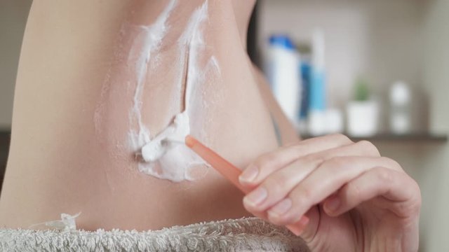 Woman shaves her armpit. Side view of attractive young girl in bathroom gently shaves her right armpit with disposable shaving blade. Close-up