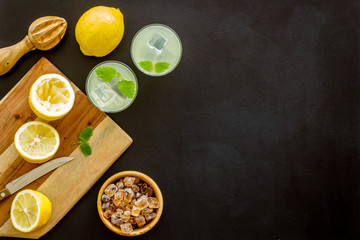 Homemade lemonade in glasses near juicer and cut lemons on black background top-down copy space