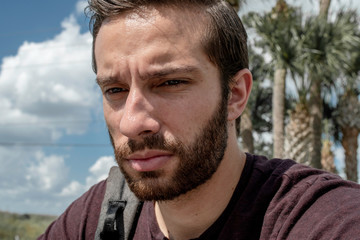 Fototapeta premium A close up of a man wearing a red shirt sits down feeling down in life as he sulks in his grief bright sunny day on a park bench
