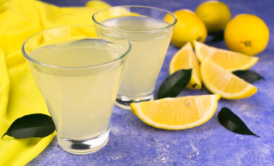 Two glasses with lemon juice and fresh lemons on a light blue background. Close-up.