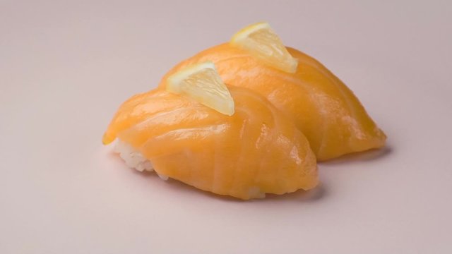 Two salmon sushi with lemon slices on the spinning pink plate.