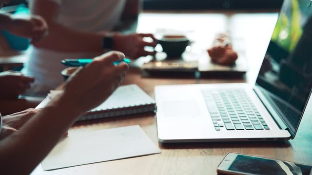 Close shot of a table with a laptop at the coworking. Coworkers team study or work together sharing a cafe table.