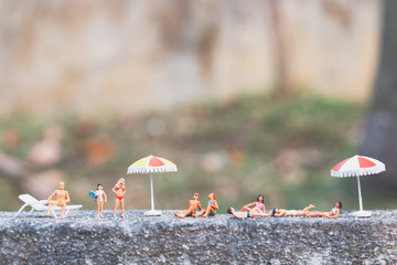 Fototapeta na wymiar Miniature people wearing swimsuit sunbathing on a rock
