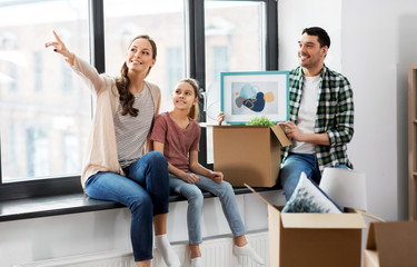 Fototapeta na wymiar mortgage, family and real estate concept - happy mother, father and little daughter with stuff in boxes moving to new home