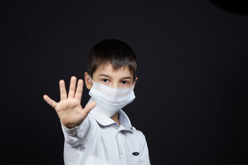 Boy in medical protective mask indicates gesture stop